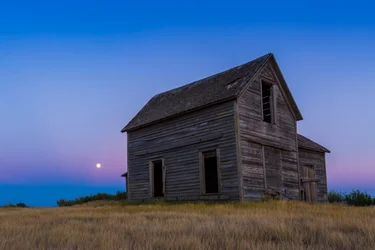 La lune presque pleine, une « Lune Bleue » du 30 juillet 2015, se levant derrière une vieille ferme rustique près de Bow Island, Alberta